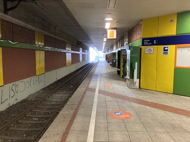 Ein Bahnsteig in Berlin Hauptbahnhof mit einem Zug auf den Schienen, beleuchtet von Deckenlampen, mit Graffiti an einer linken Wand und ein paar Gegenständen auf der rechten Seite.
