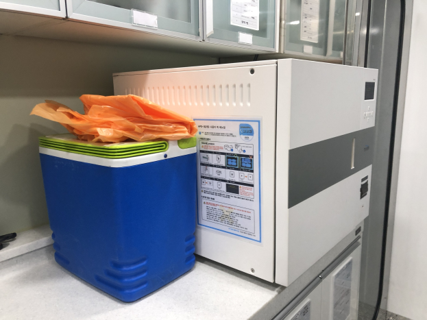 Blauer und weißer Kühler auf einer Arbeitsplatte neben einer Ultraschall-Reinigungsmaschine, mit einer Kunststoffabdeckung auf dem Kühler und anderen Gegenständen in der Nähe.