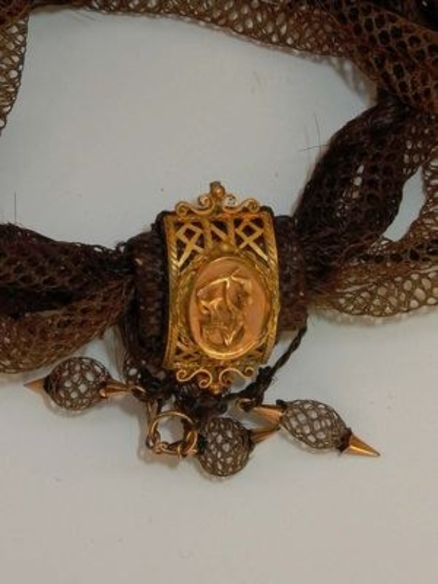 Victorianisches Gold- und Spitzenhalsband mit einem zentralen goldenen Medaillon auf einem weißen Hintergrund.