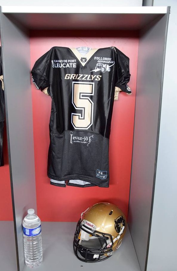 Ein Football-Trikot und ein Helm hängen an einer Spindtür, mit einer Wasserflasche auf dem Regal darunter.