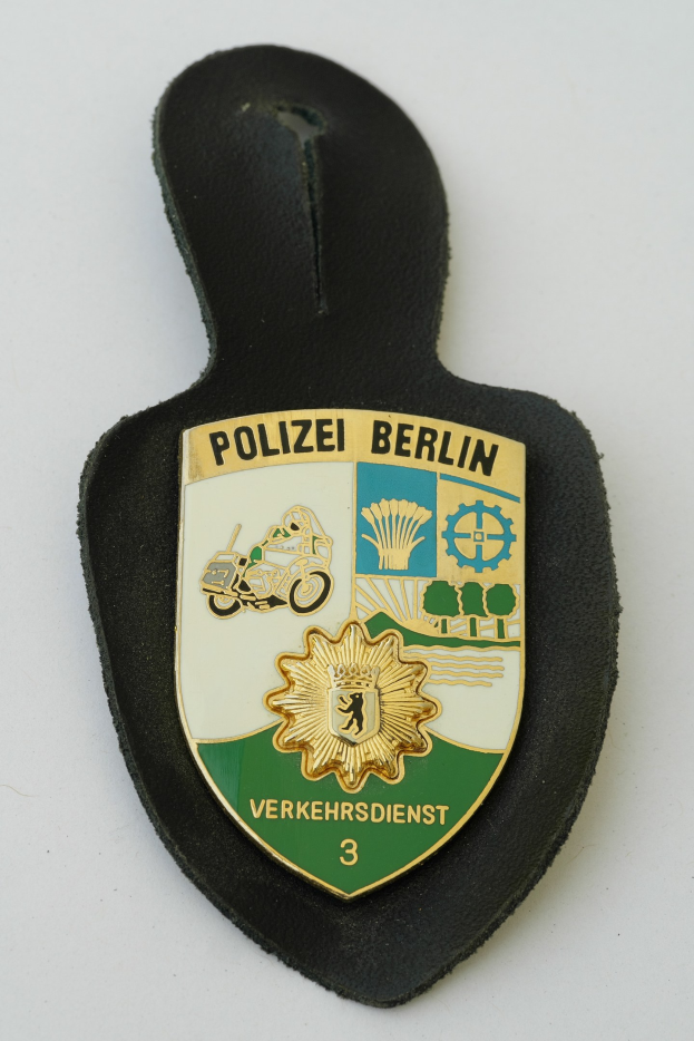 Ein schildförmiges Polizeisiegel mit "Polizei Berlin" in schwarzer fettgedruckter Schrift, das ein weißes Stern auf einem blauen Hintergrund und einen weißen Rand hat, liegt auf einer Oberfläche.
