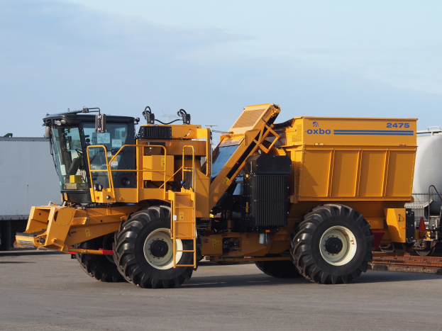 Großer gelber OXBO 2475 Radlader vor einem weißen Container auf einer Straße mit einem klaren blauen Himmel geparkt
