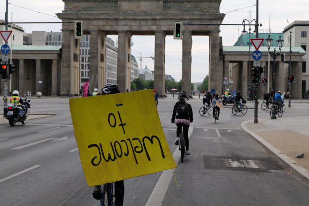 Eine Gruppe von Menschen fährt mit Fahrrädern am Brandenburger Tor in Berlin, Deutschland vorbei, wobei einer ein gelbes Schild hält.