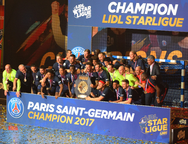 Spieler von Paris Saint-Germain feiern mit dem Ligue-1-Pokal, tragen Medaillen, vor einer Tafel mit Text und Logos, mit einem Netz auf der rechten Seite und einem Bildschirm im Hintergrund.