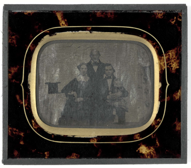 Schwarze-Weiß-Foto eines Mannes in Anzug und Krawatte und einer Frau in unbekannter Kleidung vor einem Fernseher stehend, beide mit ernsten Gesichtern.