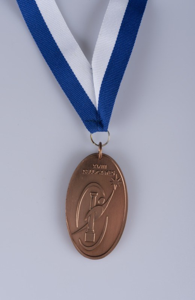 Goldene Medaille mit einem blauen und weißen Band auf einem weißen Hintergrund, mit eingravierter Schrift.