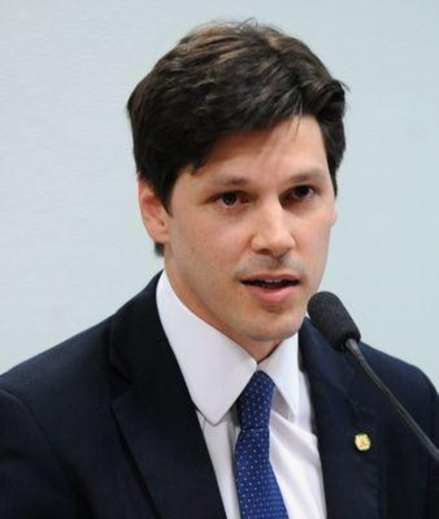 Ein Mann im Anzug und Krawatte spricht in ein Mikrofon an einem Rednerpult, wahrscheinlich um die Genehmigung eines Gesetzes durch die Regierung zu kommentieren.