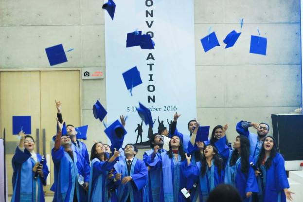 Absolventenfeier mit Studenten in blauen Roben und Mötzen, die ihre Mötze in die Luft werfen, feiernd an der University of Hyderabad.