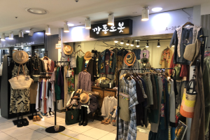 Ein Kleiderladen mit Kleiderstangen voller Kleider, Hüten, Taschen und Schuhen, beleuchtet von Deckenlampen und mit Schildern.