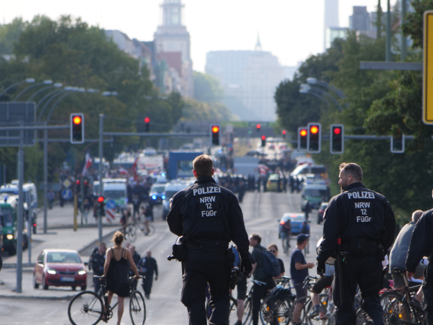 Polizeibeamte fahren mit Fahrr√°dern eine straße entlang, gesäumt von Bäumen und Geb√°uden.