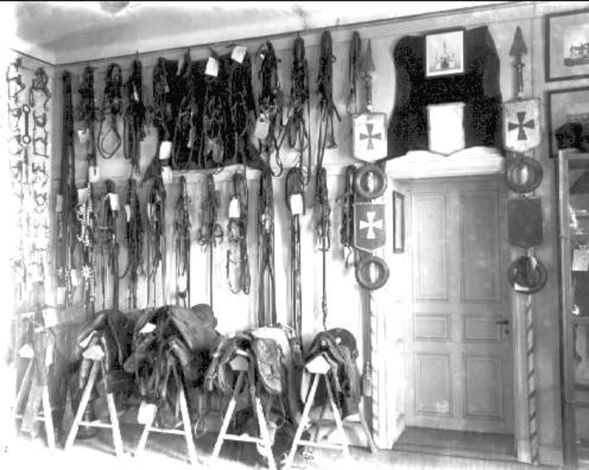 Schwarzes und weißes Foto eines Raums mit verschiedenen Reitzubehör-Artikeln, Fotorahmen und einer Tür an der Wand.