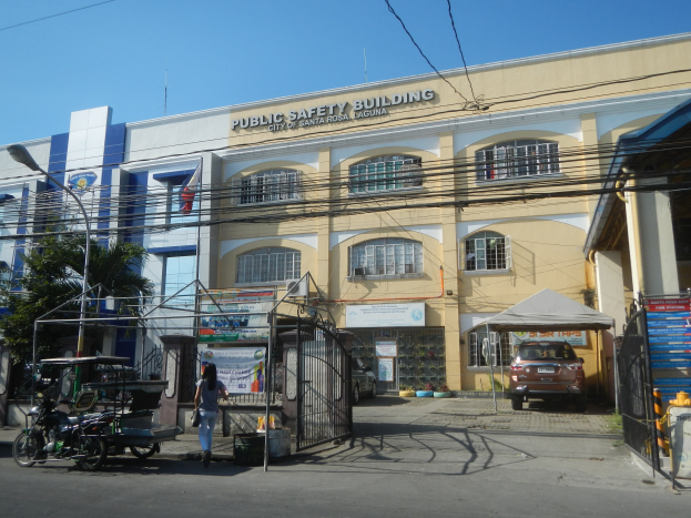 Ein mehrstöckiges Gebäude für öffentliche Sicherheit, umgeben von Bäumen, Straßeninfrastruktur, Fahrzeugen, Fußgängern und einem klaren blauen Himmel.