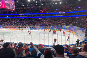Eishockeyspiel in einer großen Arena mit Zuschauern in den Rängen, eine Eisfläche umgeben von einem Zaun, eine Person mit einer Kamera auf der rechten Seite und ein Bildschirm, der 'Tulsa SunTrust Center Section 103 Row A Seat 1' anzeigt.