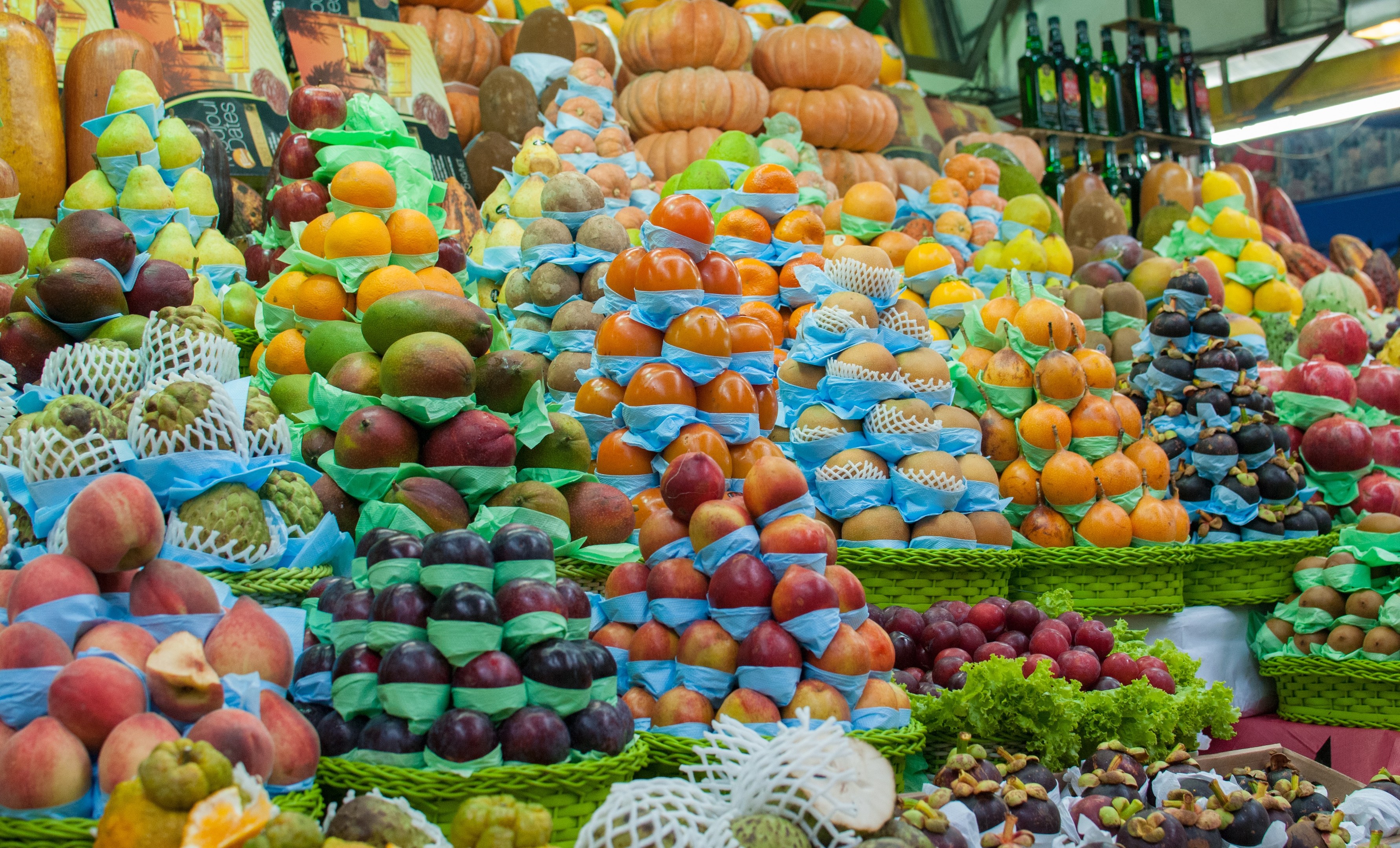 Ein Marktstand mit Äpfeln, Orangen, Birnen und anderen Obst und Gemüse, mit Flaschen auf Regalen und Deckenbeleuchtung.