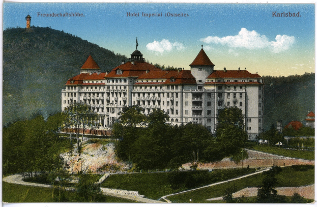 Alte Postkarte des Hotels Imperial in Karlsbad, Deutschland, zeigt ein großes Gebäude mit Fenstern umgeben von Bäumen, Pflanzen, einem Weg, Hügeln und einem bewölkten Himmel, mit Text oben.