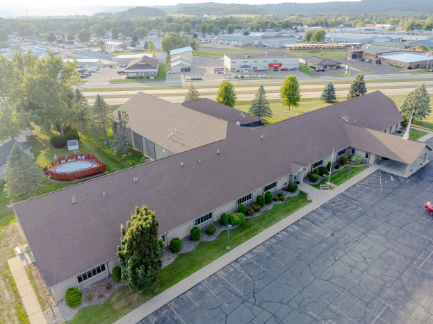Luftaufnahme eines großen Seniorenwohnheims an der University of Kentucky mit einem Parkplatz, umgeben von Grünflächen, Fahrzeugen auf der Straße, fernen Hügeln und einem klaren blauen Himmel.