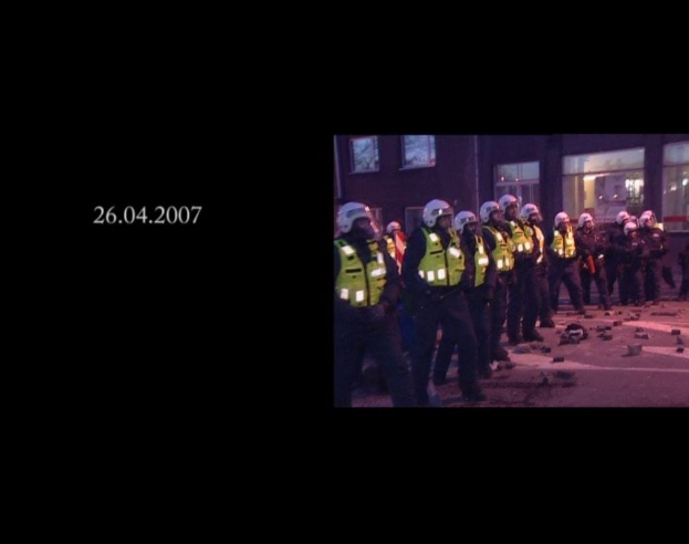 Eine Gruppe von Polizisten in Helmen und Jacken vor einem Gebäude mit Fenstern stehend, mit einem Datum auf der linken Seite.