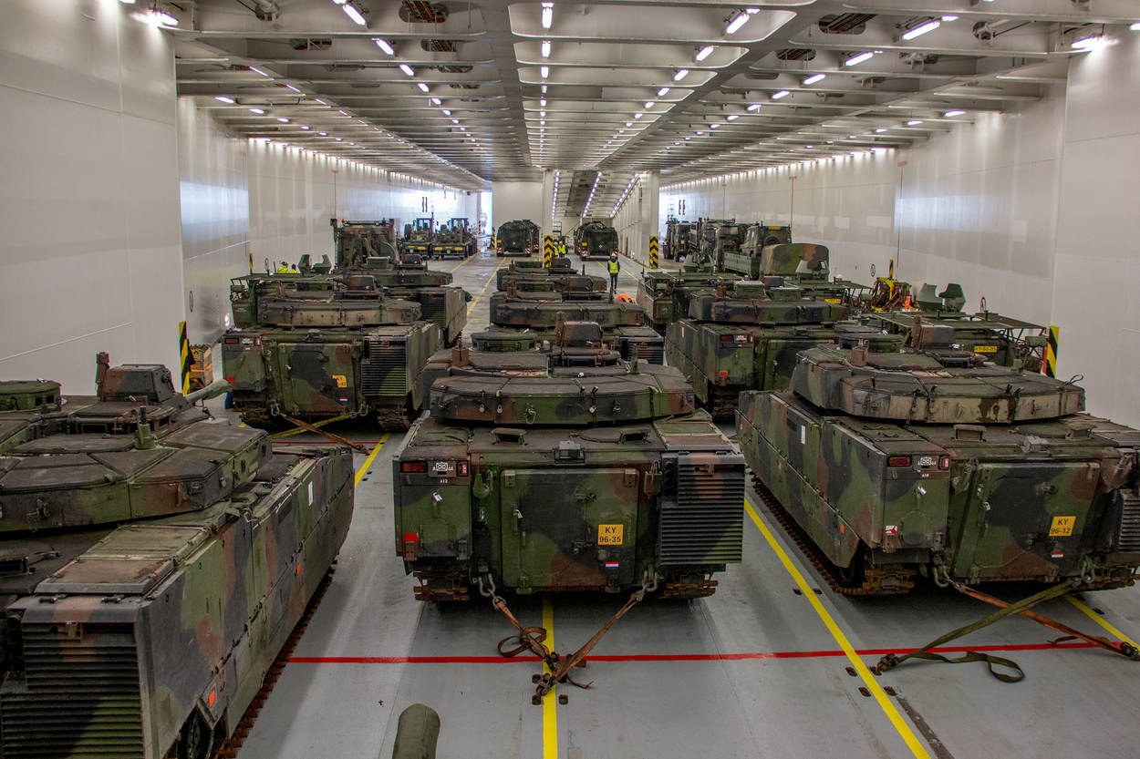 Ein großer Militärbasarraum mit Reihen von Militärpanzern, beleuchtet von Deckenlampen und von Wänden umgeben.