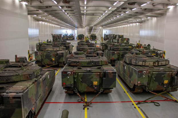 Ein großer Militärbasarraum mit Reihen von Militärpanzern, beleuchtet von Deckenlampen und von Wänden umgeben.