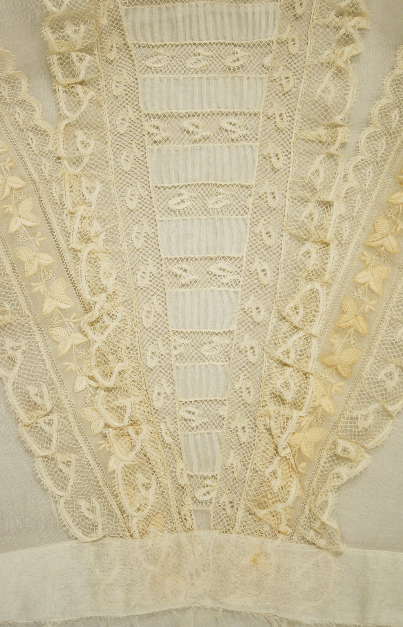Nahaufnahme eines weißen Kleides mit zarter, detallierter Spitze auf einem leichten, luftigen Stoff.