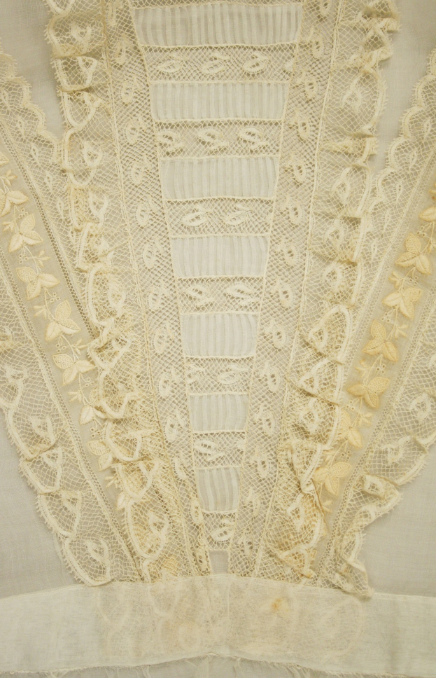 Nahaufnahme eines weißen Kleides mit zarter, detallierter Spitze auf einem leichten, luftigen Stoff.