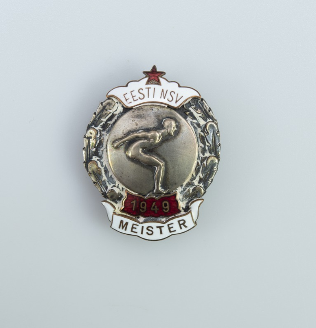 Ein silberner Abzeichen mit einem roten Stern, Emblem der Olympischen Spiele 1949 in Deutschland, mit Text in der Mitte auf einem einfarbigen Hintergrund.