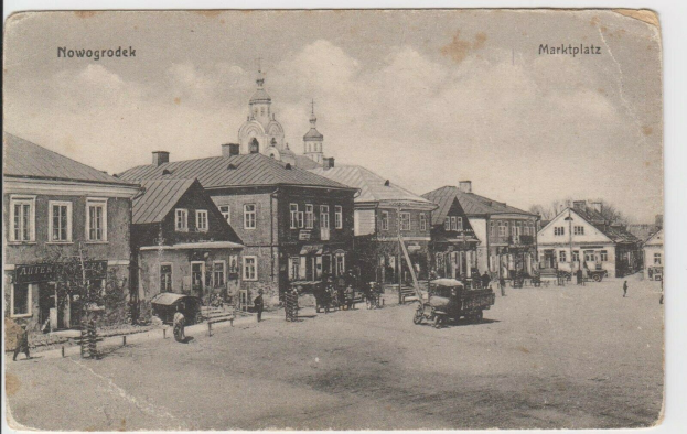 Schwarz-weißes Foto von Nowogrodziec, Deutschland's Marktplatz mit Gebäuden, Menschen, Karren, Pfählen, Bäumen und Himmel, beschriftet "Marktplatz in Nowogrodeek, Deutschland".