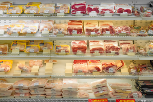 Ein gut organisierter Gemüseabteilung mit ordentlich sortierten Regalen, die verschiedene Fleischsorten und angeheftete Preisschilder zeigen.