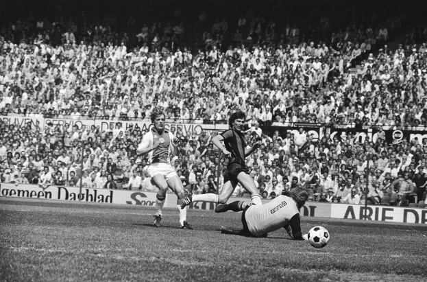 Schwarzes Foto von Männer beim Füßballspielen auf einem Feld mit Zuschauern im Hintergrund und einem Banner mit der Aufschrift "Bundesliga 1978-79 Ajax 1-1 Hannover 96".