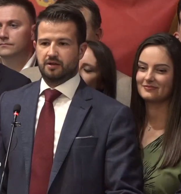 Ein Mann im Anzug spricht an einem Rednerpult mit einem Mikrofon vor einer Menge hinter einem Banner, wahrscheinlich über ein Regierungssozialmedienverbot.