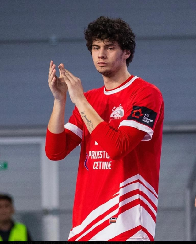 Ein Mann in einem roten und weißen Hemd klatscht in den Händen in den Vordergrund, mit einer anderen Person und einer Wand im Hintergrund; Text unten lautet 'Kopenhagen Futsal Club - Foto 1'.