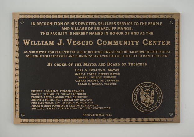 Schwarzes rechteckiges Schild mit weißer zentrierter Beschriftung, die "William J. Vesco Community Center" lautet, an einer Gebäudewand angebracht.