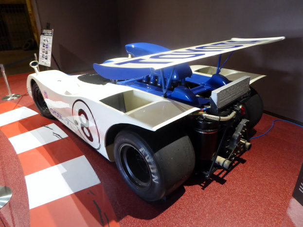 Ein wei├č-blaues Rennfahrzeug in einem museum├Ąhnlichen Setting auf der Goodwood Festival of Speed, umgeben von Absperrungen und Informationsschildern.