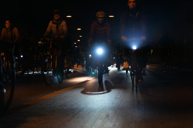 Eine Gruppe von Menschen, die nachts auf der Straße Fahrrad fahren, tragen Helme und werden von Stadtlichtern beleuchtet.