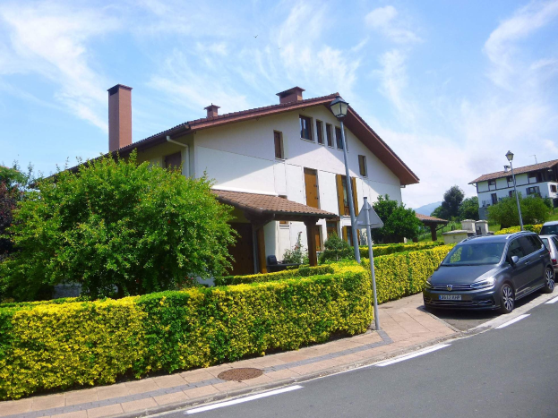 Villa zum Verkauf in Lago di Garda, Italien, mit einem Auto auf der Straße geparkt, umgeben von Grünflächen und Laternen unter einem teilweise bewölkten Himmel.
