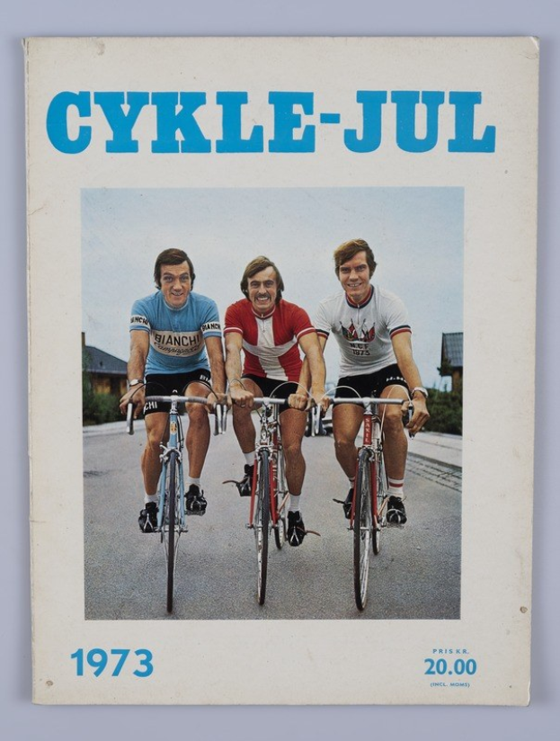 Drei Personen auf Fahrr"aden auf einer Straße mit H"usern, B"umen und einem klaren blauen Himmel, mit "Cykle-Jul 1973 - Cyclocross Magazine"-Text oben und unten.