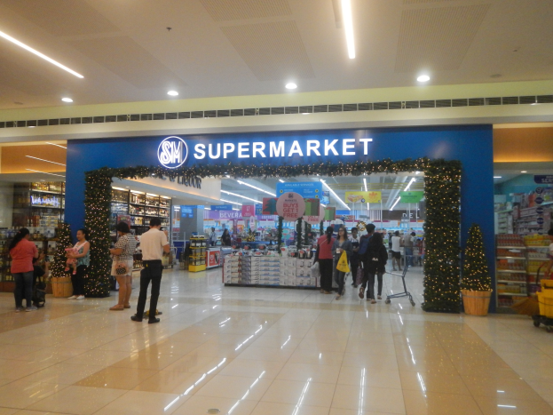 Gruppe von Menschen vor einem Supermarkt, einige halten Einkaufstaschen, mit Einkaufswagen, Topfgewächs, Regalen, Schildern und Deckenbeleuchtung.