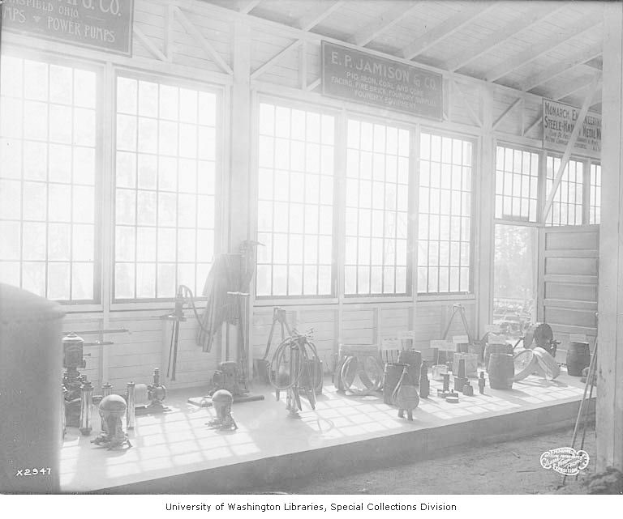 Schwarz-weiß-Foto eines großen industriellen Raums mit verschiedenen Werkzeugen, Maschinen und Texttafeln an den Wänden, beschriftet mit "P.J. Jamison & Co. Power Pumps" unten.
