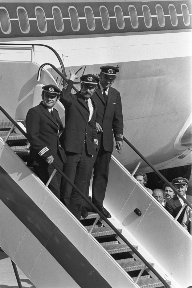 Schwarzes und weißes Foto einer Gruppe von Männern in Blazern, Krawatten und Mützen, die auf der Treppe eines Flugzeugs stehen.