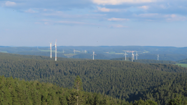Windpark mit Turbinen in einem bewaldeten Gebiet, Hügel sind im bewölkten Himmel Hintergrund zu sehen.