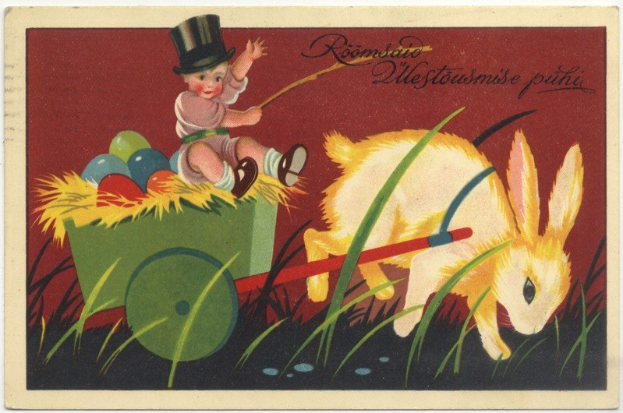 Alte Postkarte mit einem Baby in einem Zylinder, das einen mit bunten Ostereiern gefüllten Handwagen schiebt, begleitet von einem Kaninchen, mit handgeschriebenen Ostergrü├čen.