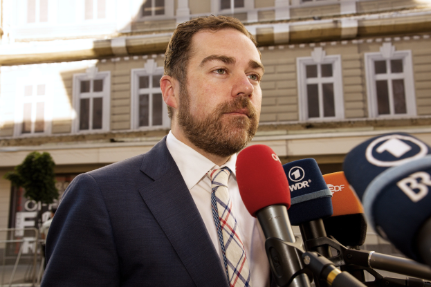 Ein Mann im Anzug spricht vor einem Gebäude zu den Medien, wahrscheinlich im Zusammenhang mit einer dreijährigen Haftstrafe.