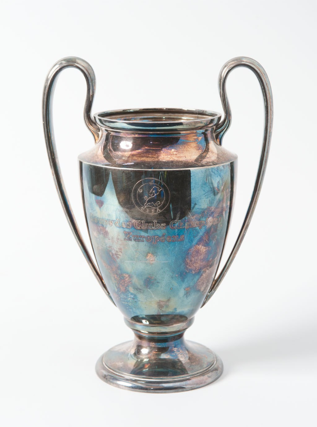 Der UEFA-Champions-League-Pokal, ein stahlerner Becher mit zwei Griffen und einem blauen und silbernen Farbschema, der mit 'UEFA Champions League' beschriftet ist, vor einem weißen Hintergrund.