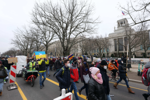 Eine große Gruppe von Menschen nimmt an einer Protestdemo in Washington, D.C. am 21. Januar 2020 teil und marschiert eine Straße entlang, wobei sie Schilder, Banner und Fahrräder trägt, vor einem Gebäude mit Schildern, Bäumen und einem klaren blauen Himmel.