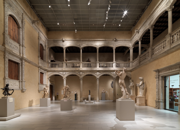 Großes Museumsgalerie mit zahlreichen Statuen und Skulpturen auf Sockeln, architektonischen Elementen wie Säulen und Geländern, Deckenbeleuchtung und einigen Besuchern.