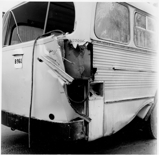 Schwarz-weiß-Foto eines Busses mit schwerer Frontschaden nach einem Autounfall, auf der Straße positioniert.