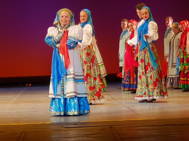 Eine Gruppe von Menschen in bunten, detaillierten traditionellen ukrainischen Kostümen, die auf einer Bühne lächeln und stehen.