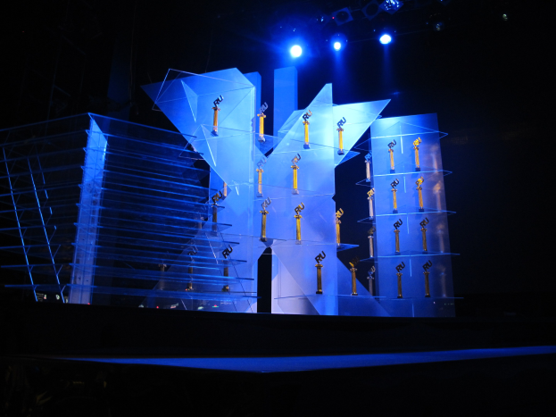 Eine Bühne für eine Preisverleihung mit dunklem Hintergrund, die von ein paar Lichtern beleuchtet wird und ein paar Gegenstände zeigt, die mit dem Event in Verbindung stehen.