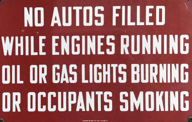 Ein rotes Schild mit weißer Schrift, das davor warnt, Autos aufzufüllen, während der Motor läuft, oder während Öl- oder Gaslampen brennen, oder wenn Insassen rauchen.