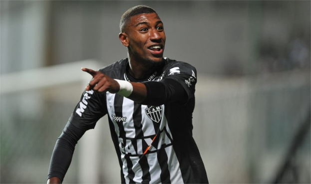 Ein Fußballspieler in einem schwarz-weißen gestreiften Trikot lächelt beim Feiern eines Tores, mit einem unscharfen Hintergrund.